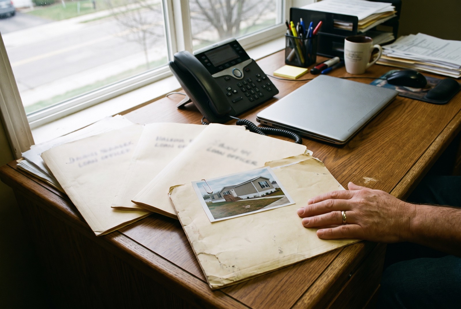 Loan files on a desk, the top one with a photo of a manufactured home clipped to it