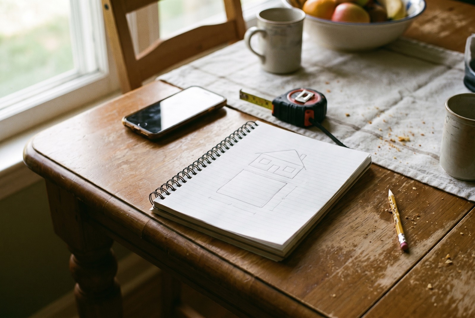 A notepad with a hand-drawn site sketch beside a phone and tape measure